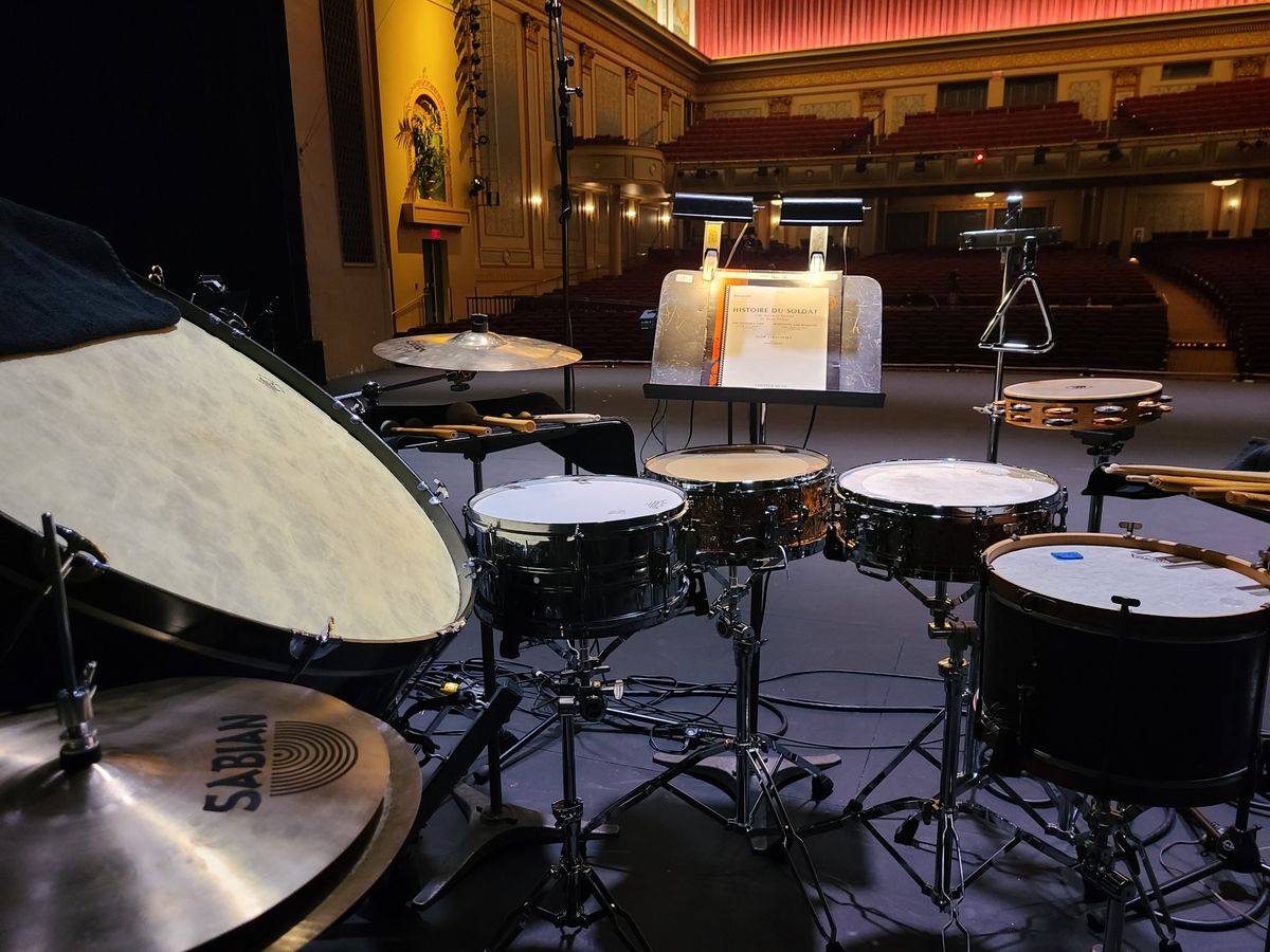 Snare drums, bass drum and cymbals set up on an empty stage, facing the hall